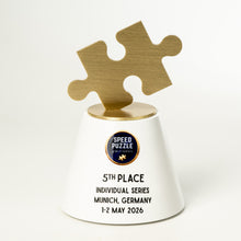 Load image into Gallery viewer, A white and gold custom trophy featuring two interlocking puzzle pieces on top, with printed text celebrating a 5th place finish in Munich, Germany, on a clean white background.