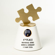 Load image into Gallery viewer, A white and gold Speed Puzzle trophy with a brushed gold puzzle piece on top, standing on a white surface against a light gray background. The base is printed with the text '4TH PLACE INDIVIDUAL SERIES MUNICH, GERMANY 1-2 MAY 2026'.