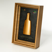 Load image into Gallery viewer, A framed gold bottle presentation on a light gray background. The bottle is mounted on a dark textured backing inside a wooden frame with a clear front cover.
