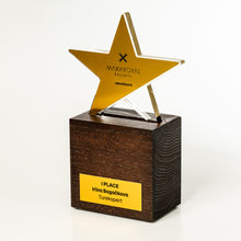 Load image into Gallery viewer, A modern award trophy featuring a polished gold star-shaped top with the 'MAXXROYAL RESORTS navodours' logo, mounted on a dark brown wood-grain square pedestal with a yellow nameplate.