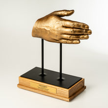 Load image into Gallery viewer, Gold hand sculpture on a black stand with a wooden base against a white background