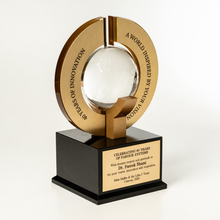 Load image into Gallery viewer, A custom corporate trophy featuring a gold-toned circular ring with engraved text, surrounding a clear glass sphere, mounted on a black rectangular base with a gold personalized nameplate.