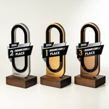 Load image into Gallery viewer, Three award trophy stands for the 2026 Roomy Cup Stage 1, arranged from left to right in 2nd place, 1st place, and 3rd place. The trophies feature a modern arch design with black and metallic gold/silver panels, mounted on dark wood bases.